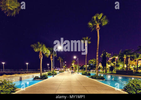 Vista notte di promenade alley con acqua e palme sul lato. La gente a piedi. Copia negativo spazio, luogo di testo. Limassol, Cipro Foto Stock