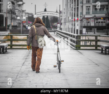 Un singolo uomo vestito con un abito vecchio sul terrapieno con la bicicletta Foto Stock