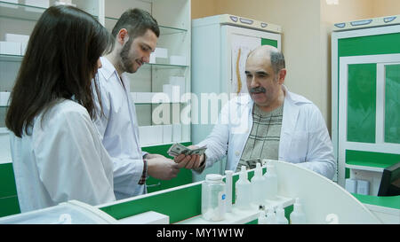 Senior farmacista dando stipendio in dollar ai suoi giovani colleghi in farmacia Foto Stock