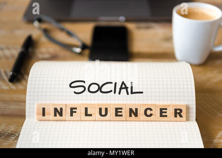 Primo piano su notebook su tavola di legno sfondo, concentrarsi sui blocchi di legno con lettere che Social Influencer testo. Foto Stock