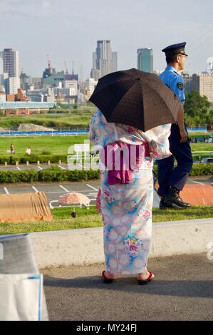 Una donna giapponese che indossa un tradizionale Yukata colorati con fiori e un ombrello per protezione solare durante un estate Matsuri festival in Osaka Foto Stock