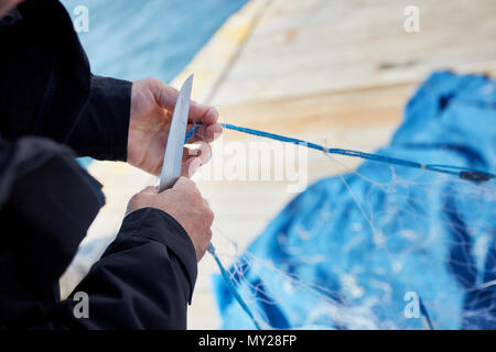 Le mani di un pescatore di riparazione di una rete da pesca con un coltello sul porto Foto Stock