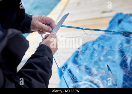 Fisherman riparazione di una rete da pesca con un coltello sul porto Foto Stock
