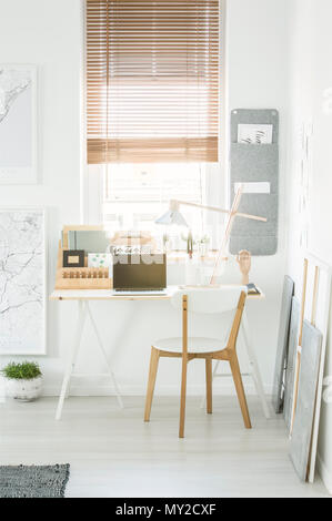 Home office desk con notebook, lampada portatile e in piedi sotto la finestra con persiane in bianco living room interior Foto Stock