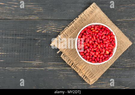White ciotola riempita con barberries fresca su un letto di sacco e di vuoto sullo sfondo di legno, vista dall'alto Foto Stock