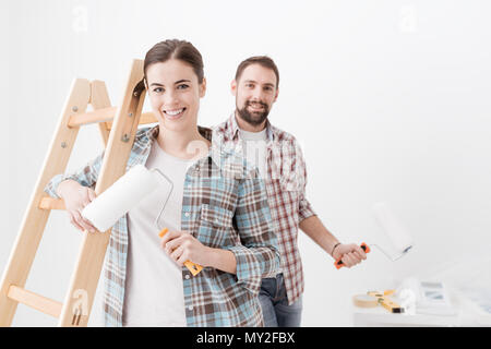 Felice coppia giovane pittura la loro nuova casa, essi sono sorridente e trattenere i rulli di verniciatura Foto Stock