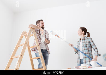 Giocoso coppia felice pittura la loro nuova casa e divertirsi insieme, stanno giocando con i rulli di verniciatura Foto Stock