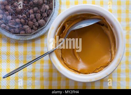 Pentole & Co pot artigianale di caramello salata brulee con un cioccolato & caramello top hat pudding con cucchiaio impostato su giallo e bianco a scacchi tovagliolo tovagliolo Foto Stock