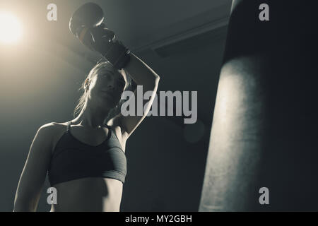 Giovane donna facendo boxing training presso la palestra, indossa guanti di punzonatura e sorridente Foto Stock