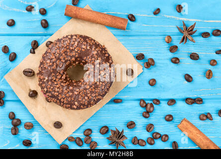 Ciambella di cioccolato con chicchi di caffè sparsi su un tavolo blu, vista dall'alto Foto Stock