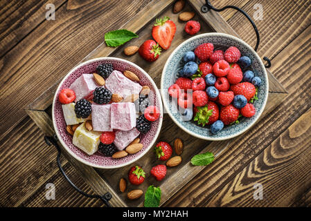 Turkish Delight con dadi e bacche di coppe in ceramica su sfondo di legno, vista dall'alto Foto Stock
