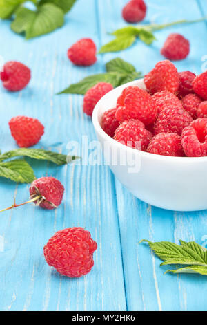 Fresco di lampone rosso con un recipiente pieno di bacche e foglie sparse su un sfondo di legno Foto Stock