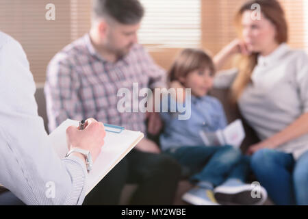 La mano di un professionista psicoterapeuta familiare la scrittura di note nella parte anteriore di una coppia con un bambino in uno sfondo sfocato durante una consultazione Foto Stock