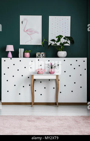 Vecchio stile, telefono rosa e un impianto su un elegante, retro tavolo laterale da un bianco polka dot parete in un buio living room interior Foto Stock