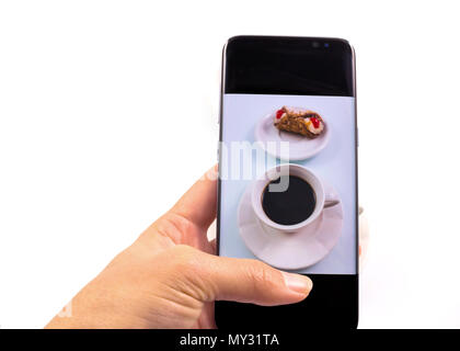 Le mani di scattare la foto, caffè e dolce cookie con uno smart phone in sfondo bianco. Foto Stock