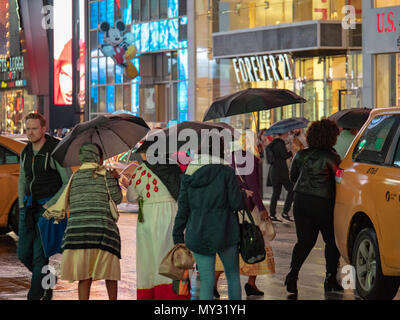 NEW YORK, NY - 16 Maggio 2018: Times Square i turisti a piedi passato negozi al dettaglio in un giorno di pioggia ombrelli azienda Foto Stock