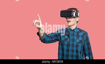 Stupiti giovane con vr auricolare tenta di toccare la realtà. studio shot, isolato su sfondo rosa. Foto Stock