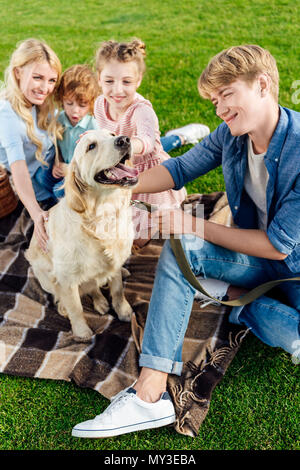 Angolo di alta vista di felice famiglia giovane con il golden retriever dog sitter su plaid in posizione di parcheggio Foto Stock