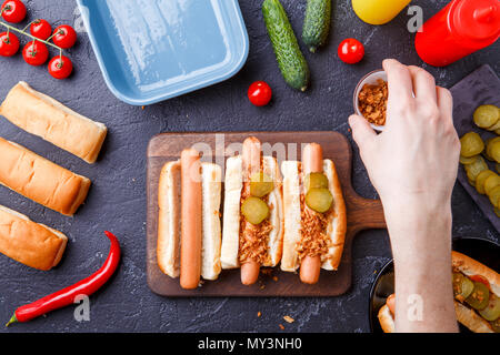 Immagine da sopra dell'uomo facendo hotdog sul bordo di taglio sul tavolo con salsicce Foto Stock