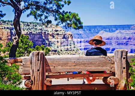 Tourist seduta sul banco di legno nella parte anteriore del Grand Canyon paesaggio, Arizona, Stati Uniti d'America Foto Stock