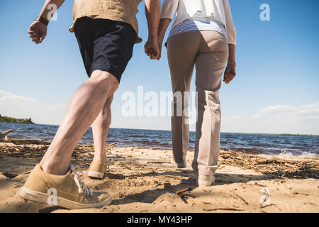 Ritagliato colpo di coppia senior tenendo le mani e camminare sulla spiaggia di sabbia Foto Stock