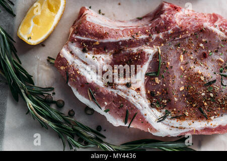 Vista ravvicinata di materie ribeye con spezie, limone e rosmarino sulla carta da forno Foto Stock