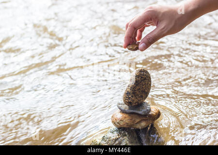 Mettendo mano pietra su pietra di impilamento sul lungofiume. Le pietre sono impilati sul lato del fiume. Foto Stock