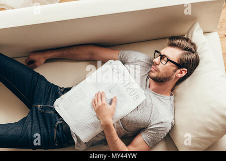 Giovane uomo caucasico dormire con giornale sul divano di casa Foto Stock