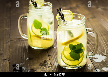 Il freddo limonata fresca cocktail mojito con ghiaccio, succo di limone e foglie di menta in Mason Jar sul rustico in legno scuro dello sfondo. Concetto di estate. Foto Stock
