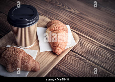 Due cornetti e caffè-to-go sul vassoio su sfondo di legno Foto Stock
