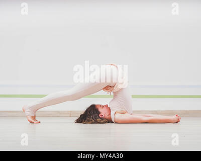 Giovane donna graziosa pratica yoga alla luce studio minimalista sala di classe. Concentrato bella ragazza in Halasana aratro. Foto Stock