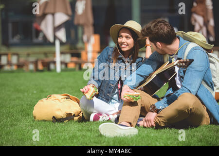 Coppia di viaggiatori in cappelli con zaini e chitarra azienda panini Foto Stock