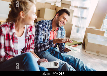 Sorridente coppia giovane conteggiare denaro nella nuova casa Foto Stock