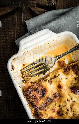 Mangiare le lasagne italiane con la forcella della scura sullo sfondo di legno Foto Stock