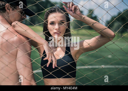 Ritratto di donna sportive guardando telecamera attraverso net pur poggiando sull'uomo Foto Stock