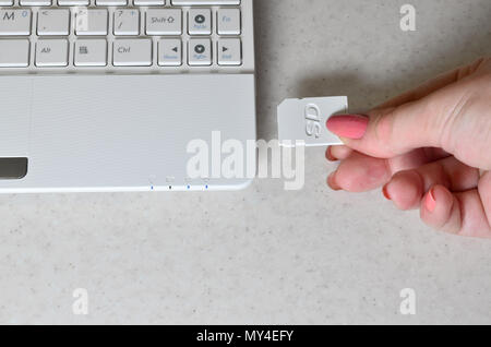 Una femmina di inserti in mano un bianco compatto scheda SD in ingresso corrispondente al lato del netbook bianco. La donna utilizza moderne tecnologie per memorizzare m Foto Stock