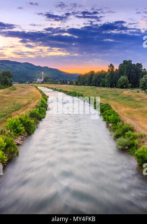 Vista verticale del moto sfocata Nisava fiume di Pirot e distante il vecchio stabilimento durante la vivace, tramonto colorato Foto Stock
