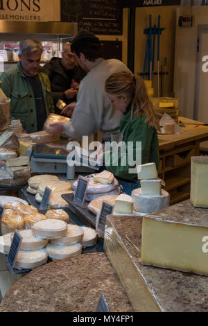 Una donna su un contatore di formaggio al mercato stallo a Borough Market nel centro di Londra. Servire su una bancarella vendendo i prodotti lattiero-caseari su un mercato in stallo. Foto Stock