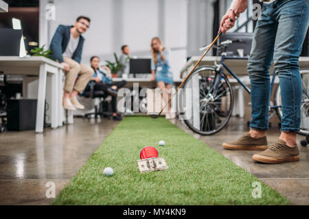 Immagine ritagliata di persone a giocare a minigolf presso un ufficio moderno Foto Stock