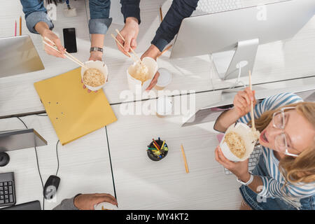 Vista dall'alto di mani tagliate con cibo tailandese sulla tavola di lavoro presso un ufficio moderno Foto Stock