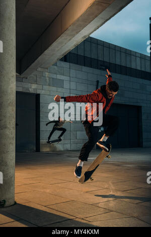 Skateboarders di eseguire trucchi di salto insieme alla posizione urbana Foto Stock