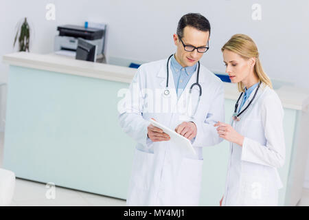 Due medici in camici con la compressa a discutere la diagnosi in clinica Foto Stock