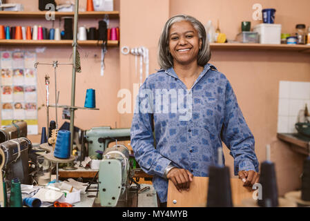 Ritratto di un sorridente coppia sarta in piedi da una tabella nel suo tessuto surround workshop dalla apparecchiatura di cucitura Foto Stock