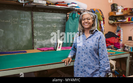 Ritratto di un sorridente coppia sarta in piedi da una tabella nel suo tessuto surround workshop dalla apparecchiatura di cucitura Foto Stock