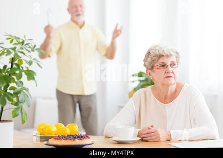 Triste senior donna litigare con suo marito in piedi di sfondo sfocato Foto Stock