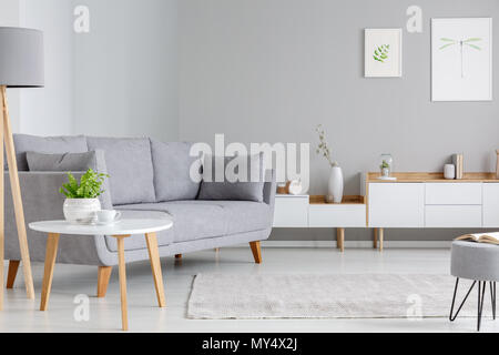 Tabella accanto al divano grigio in scandi living room interior con poster sopra l'armadio. Foto reale Foto Stock