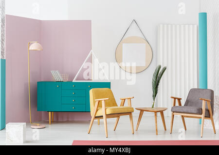 Grande triangolo bianco posto su un turchese credenza con libri in interni luminosi con due poltrone in legno tavolo finale e fresche piante in vaso Foto Stock