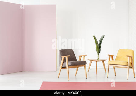 Due grigio e giallo poltrone e piccolo tavolo in legno con foglie in vaso di vetro in piedi nella luminosa sala interna Foto Stock