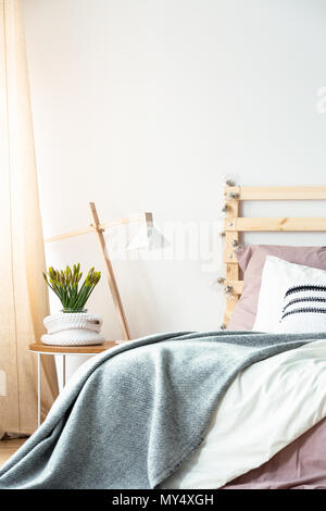 Grigio un lenzuolo sul letto in luminosa camera da letto minimo interno con lampada e impianto sul tavolo. Foto reale Foto Stock