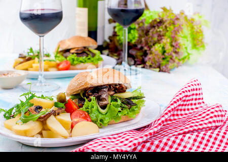 Deliziosi hamburger vegetariano e patate per tre. Insalata. Pranzo e vino. Sfondo di luce e spazio per il testo. spazio copia Foto Stock